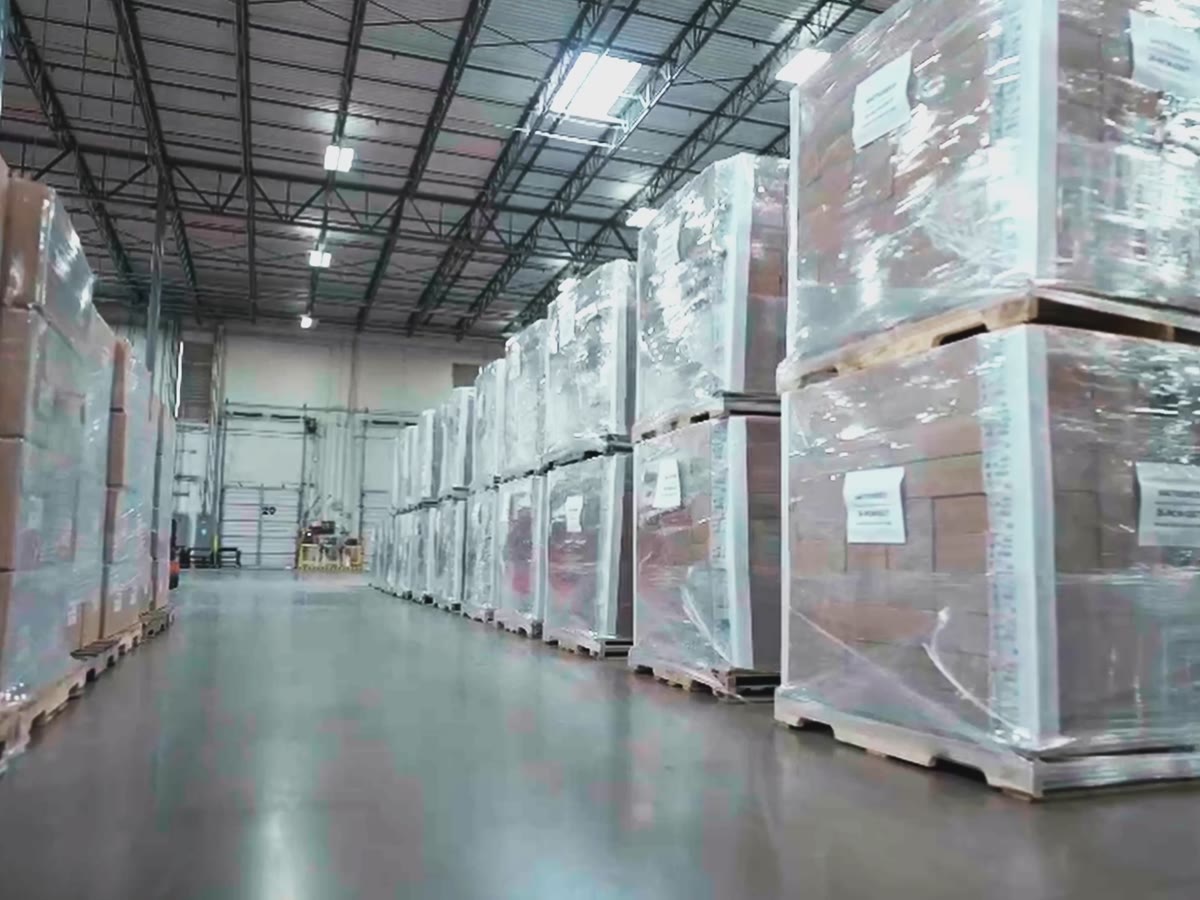 An aisle of shrink-wrapped, labeled pallets staged for retail distribution in a Productiv warehouse