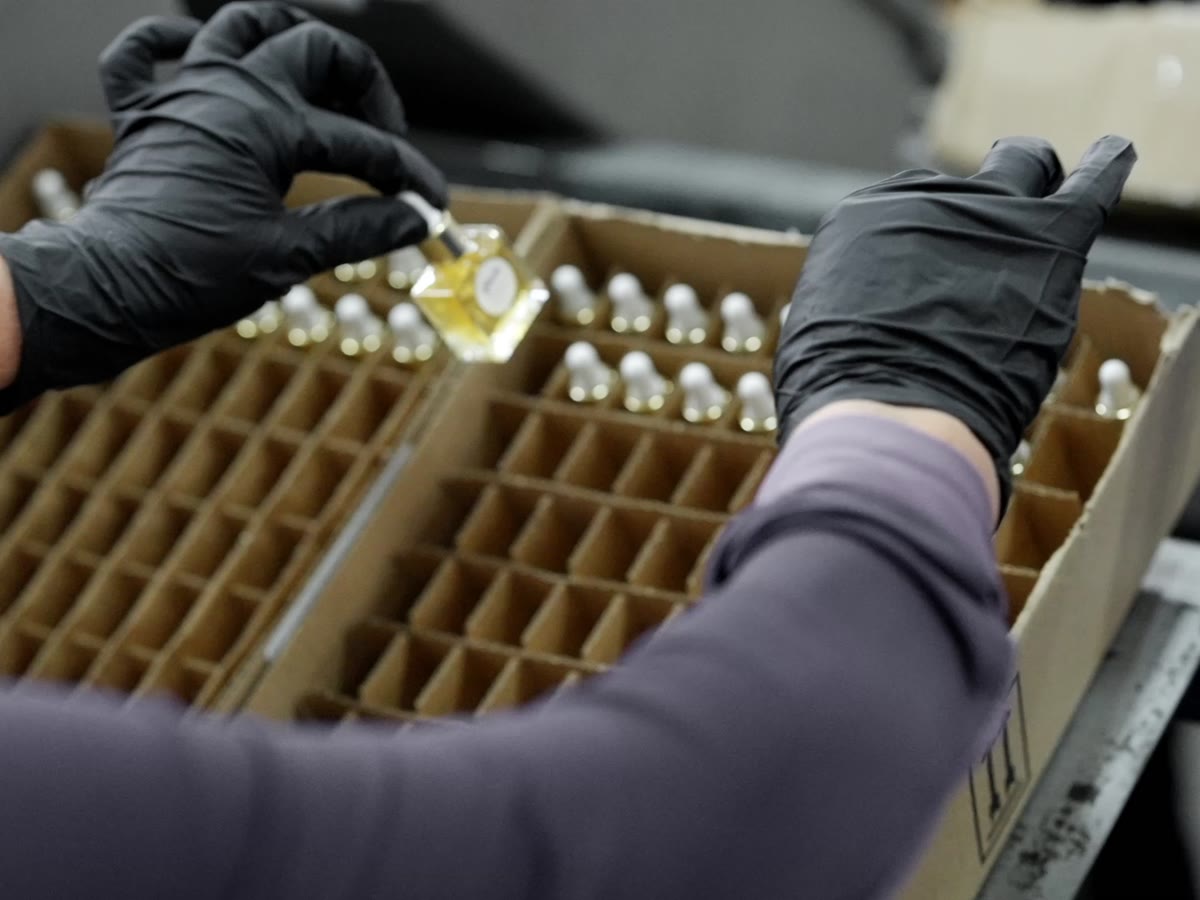 A gloved Productiv operator placing fragrance vials into a divided corrugated insert on a beauty kitting line