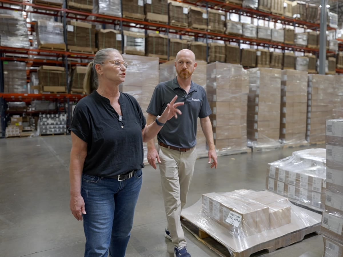 Productiv CFO and co-owner Paul Baker walking the warehouse floor with a team member between rows of labeled pallets