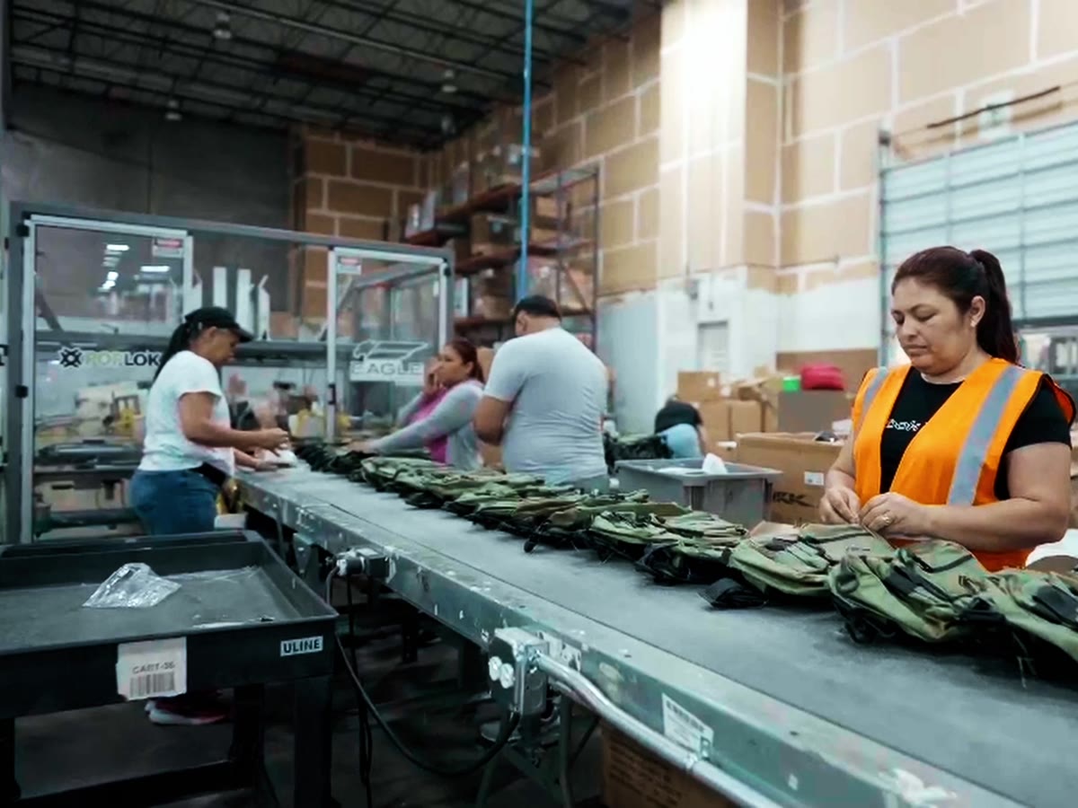 A Productiv operator in a safety vest kitting outdoor tackle bags on a conveyor line inside the warehouse