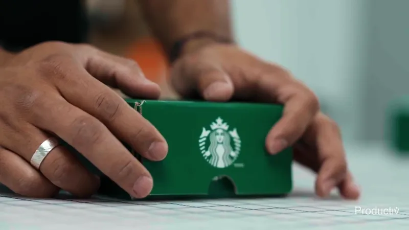 Hands closing a beverage brand's green gift box on a Productiv packout table